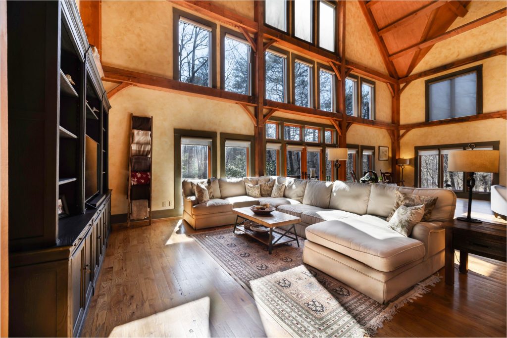 Large living room with timber framing, a wrap-around beige sectional sofa, and a wall of tall windows.