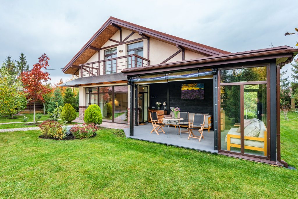 A two-story house with a partially enclosed patio featuring outdoor furniture and a large lawn in the foreground.