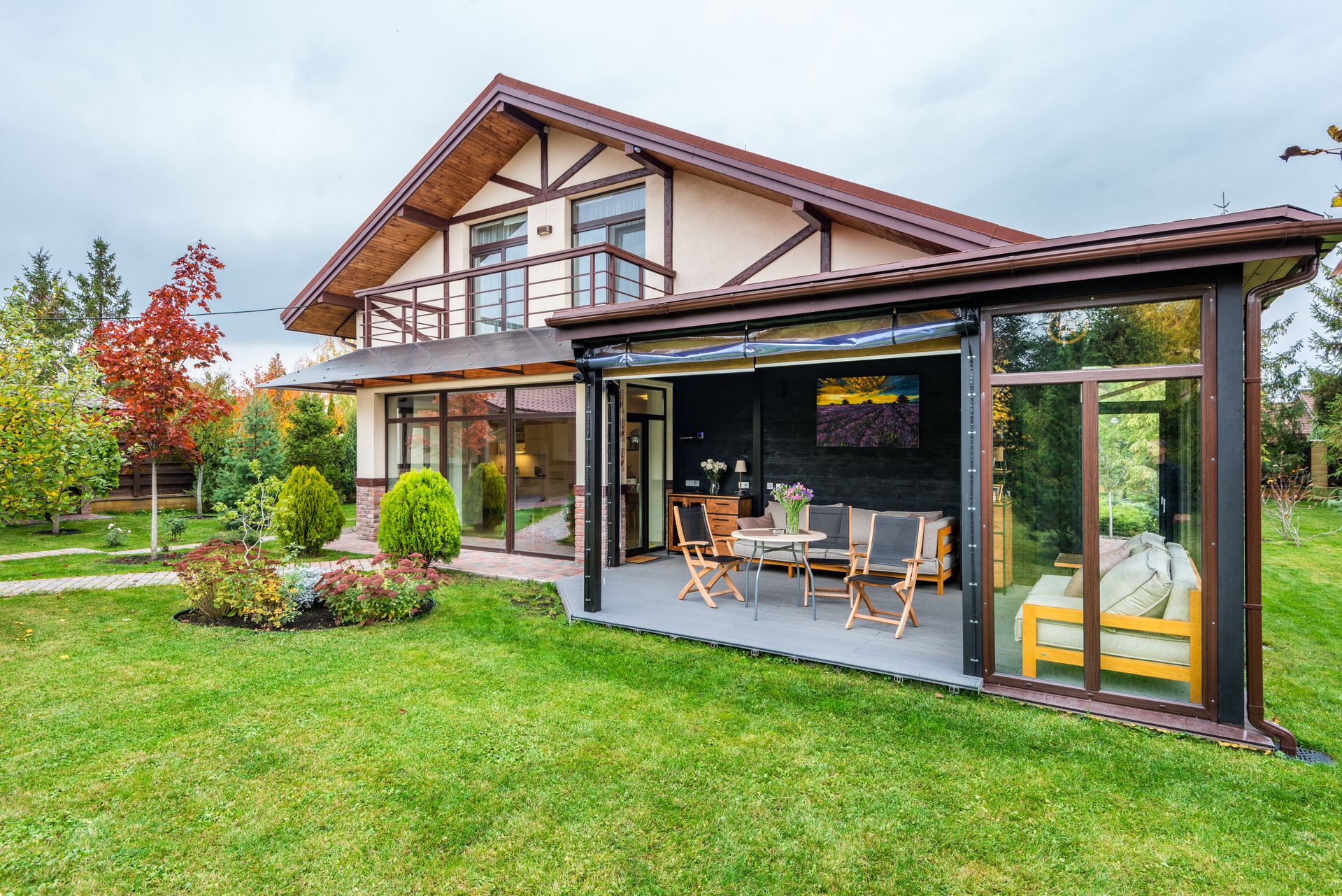 A two-story house with a partially enclosed patio featuring outdoor furniture and a large lawn in the foreground.