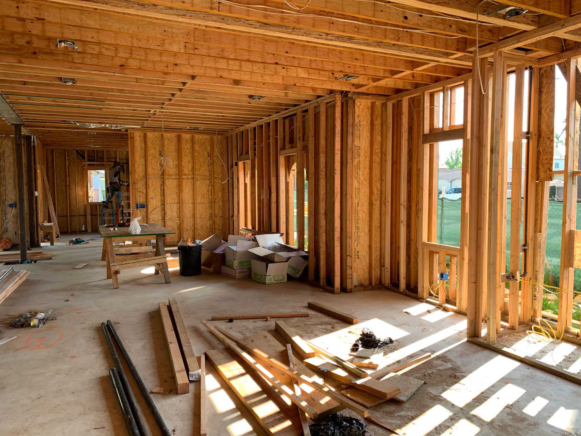 Interior of a house under construction with exposed wooden wall framing, floor joists, and scattered lumber.