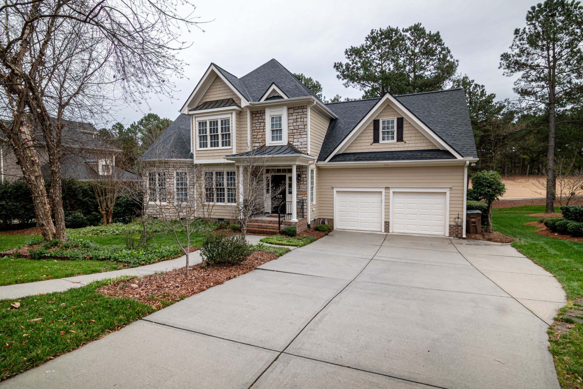 A two-story suburban house with stone and tan siding, a dark shingled roof, and an attached two-car garage.
