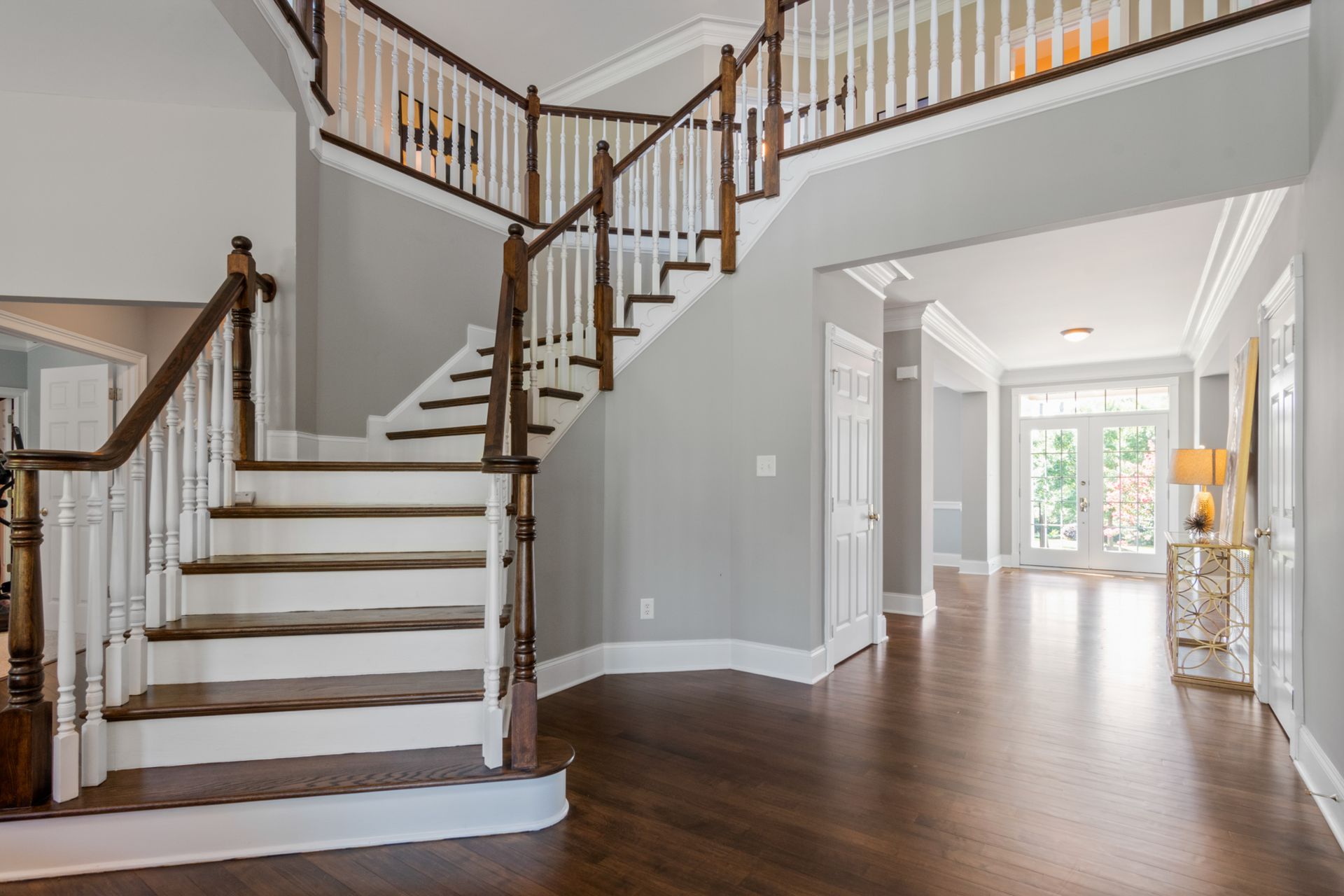 Foyer with a wood and white staircase, dark hardwood floors, and a view into a hallway with a glass console table and lamp.