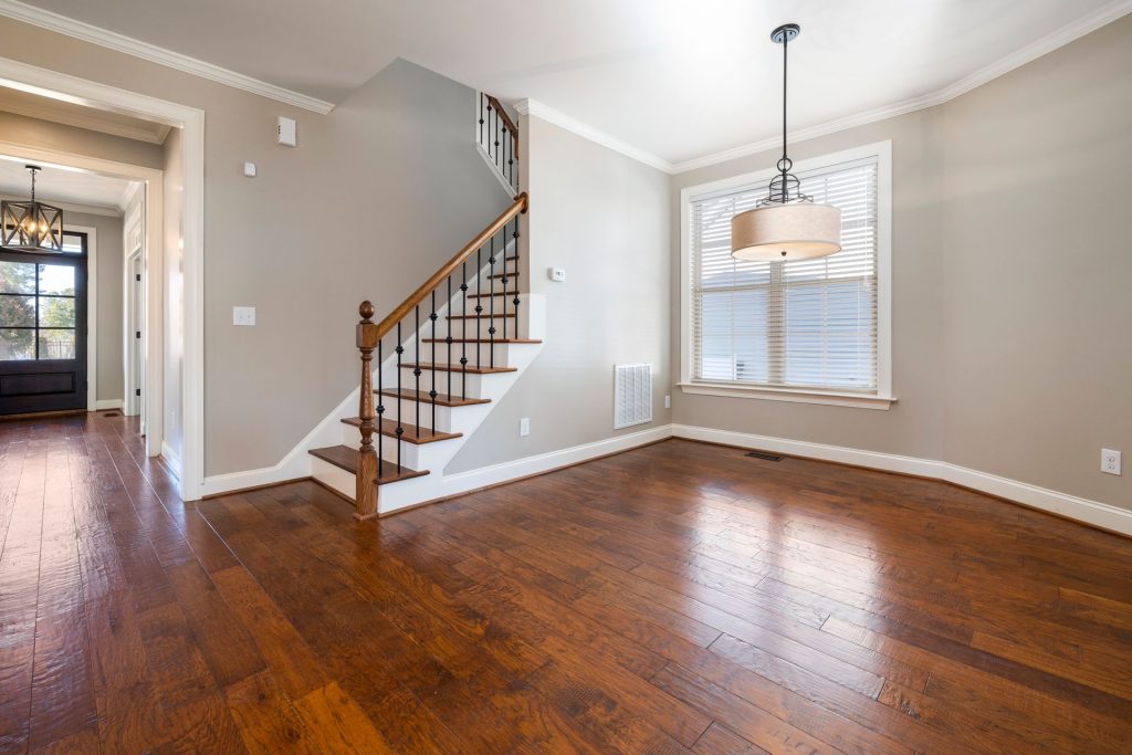 Empty room with hardwood floors, a staircase with a wooden handrail and black metal balusters, and a drum pendant light hanging by a window.