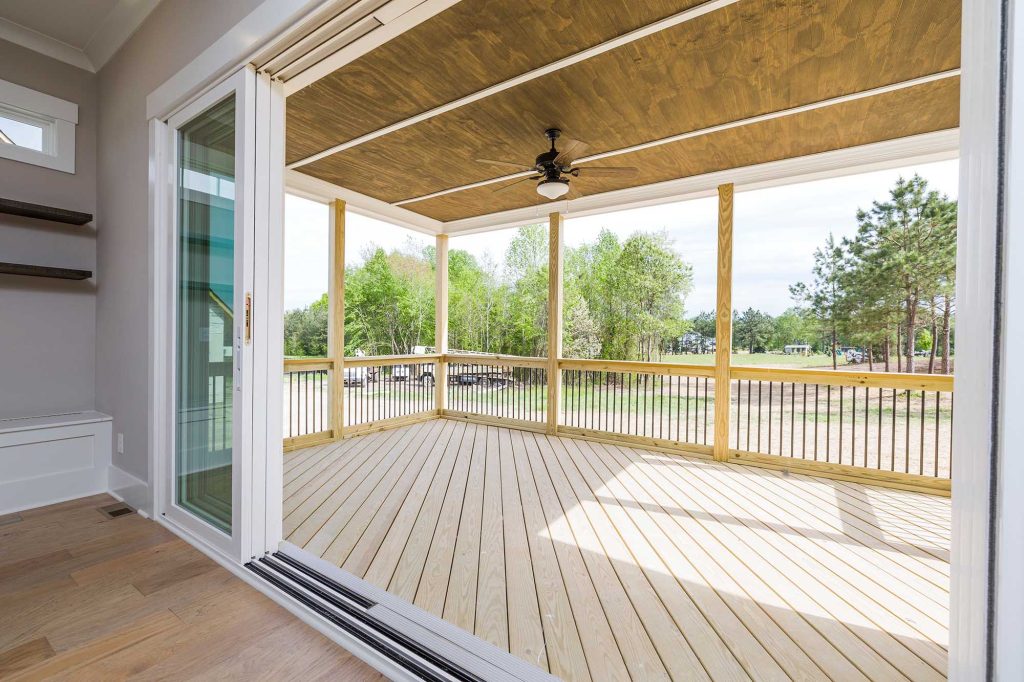 A covered wooden deck with a ceiling fan, accessed through open sliding glass doors from an indoor room.