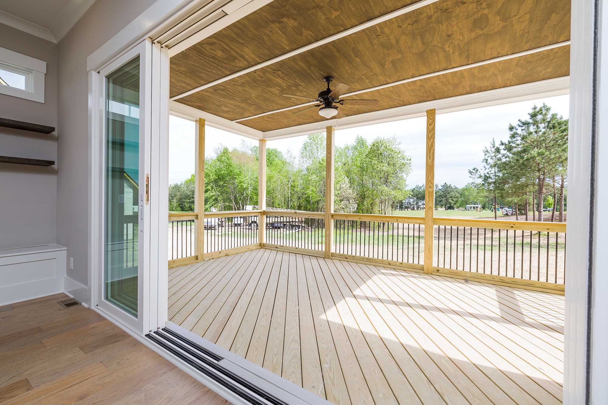 A covered wooden deck with a ceiling fan, accessed through open sliding glass doors from an indoor room.