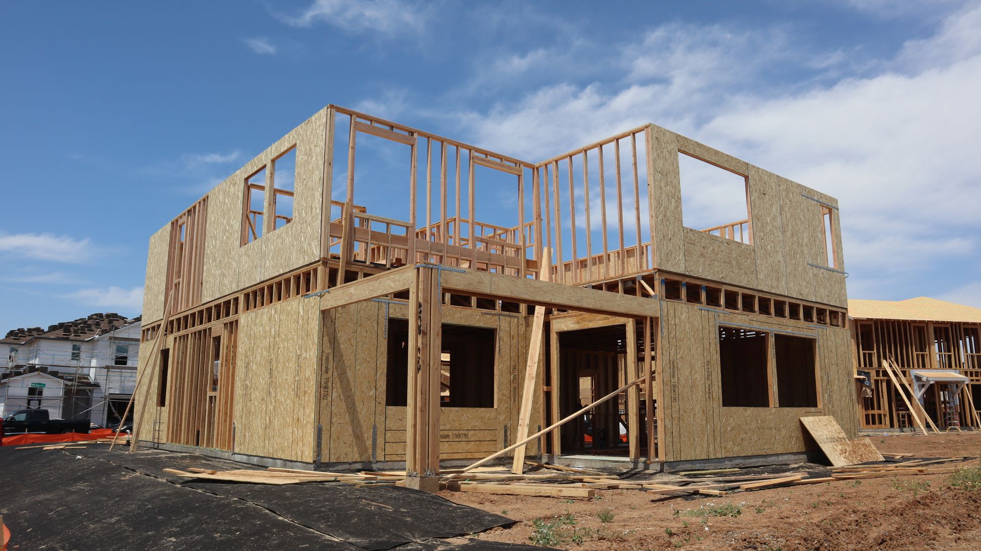 Two-story house under construction with exposed wooden framing and plywood walls.