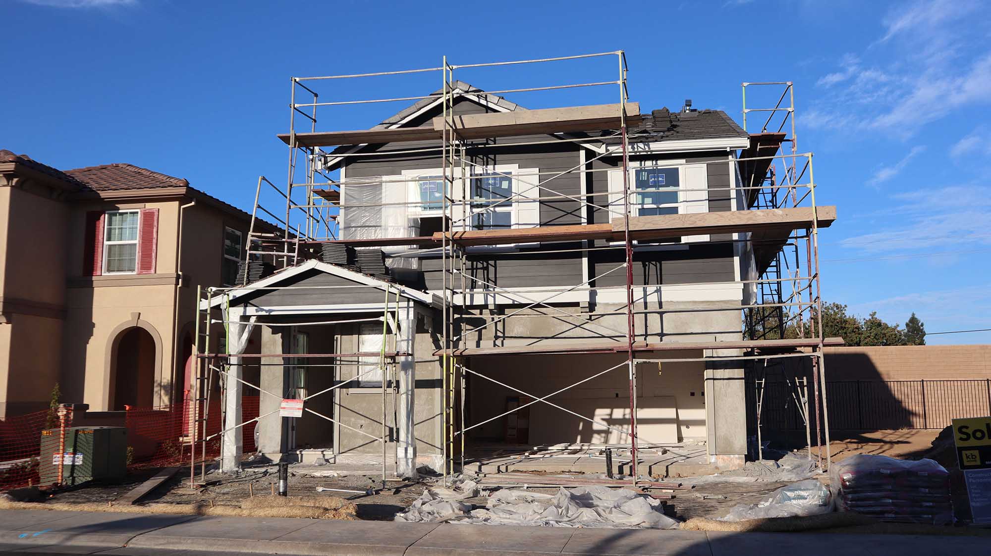 A two-story house under construction, surrounded by scaffolding and plastic sheeting.