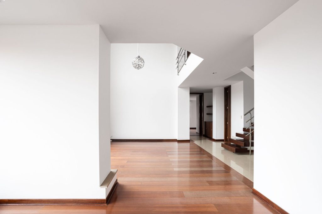 An open-plan interior with white walls, hardwood flooring, and a wooden staircase with a metal railing.