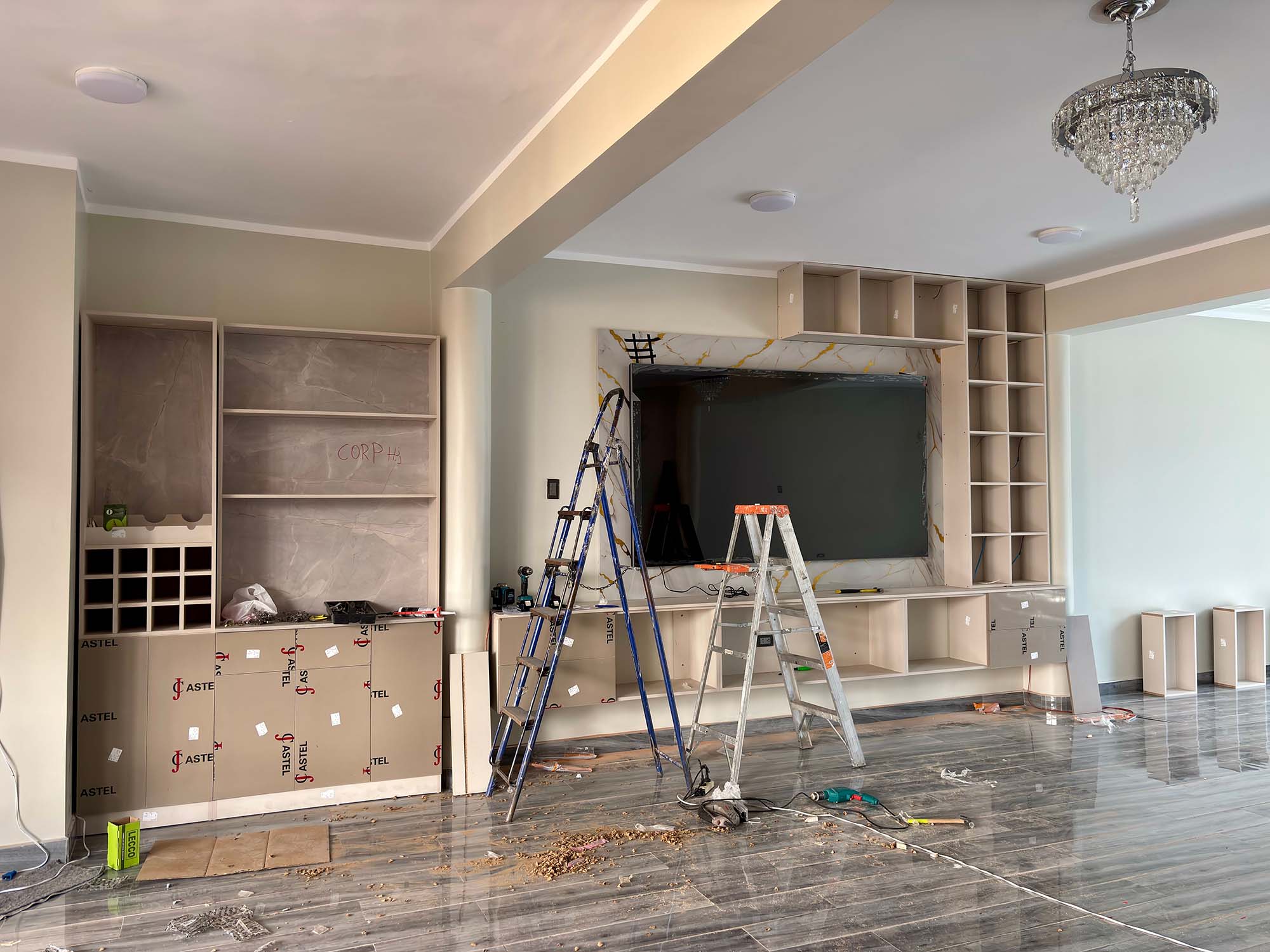 A room under construction featuring custom built-in cabinetry and a wall-mounted television, with two step ladders and tools on the floor.