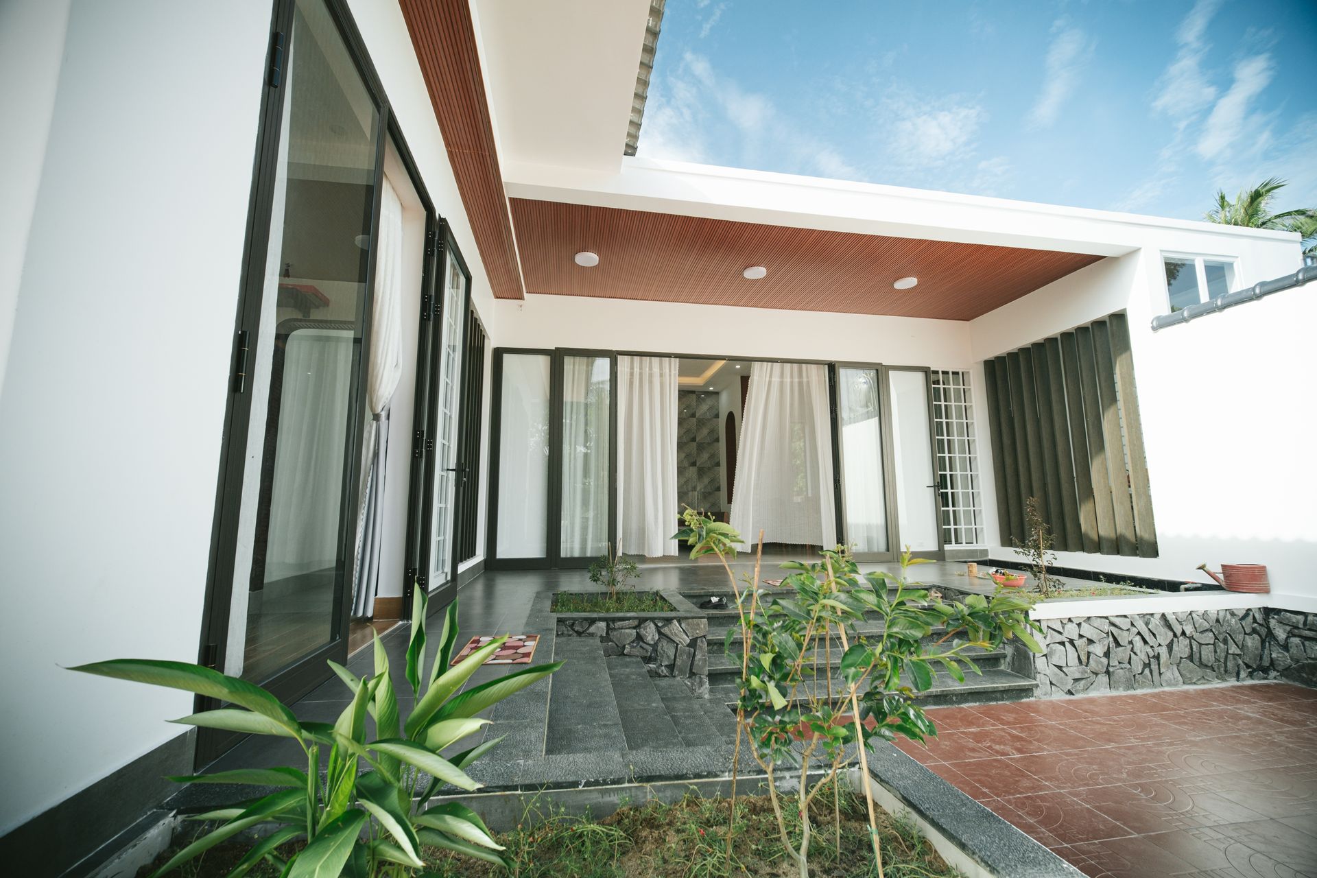Modern custom home exterior featuring a covered patio, glass sliding doors, and terraced stone steps leading to an interior living space.