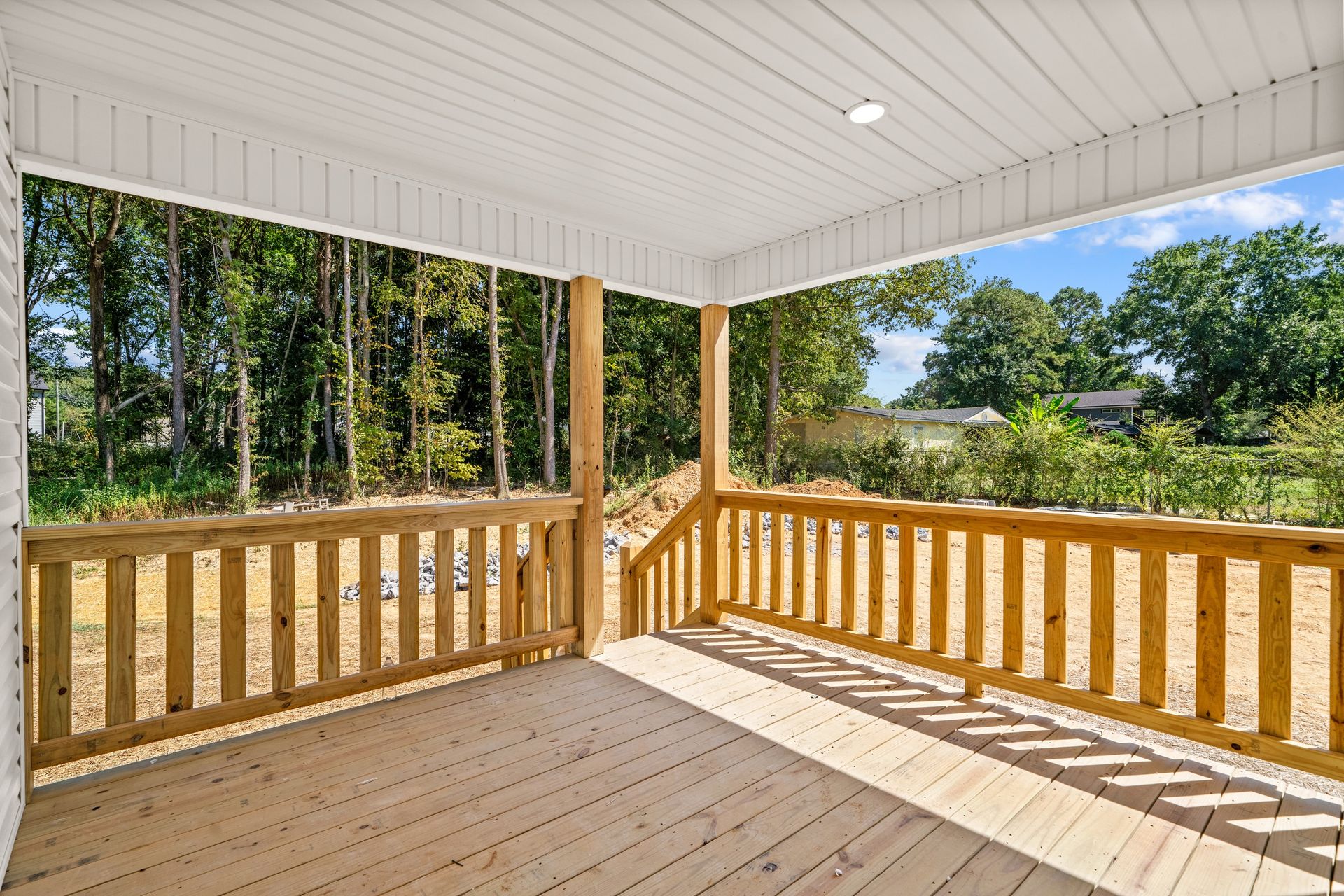 A covered wooden deck with a railing overlooking a backyard with trees.